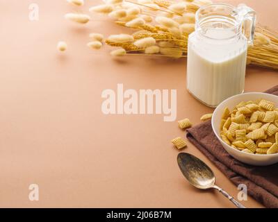 Sur fond beige, un bol avec des oreillers de grains entiers, une cuillère, du lait dans un pot et un décor - un bouquet de céréales. Tons beige, il y a un endroit à se Banque D'Images