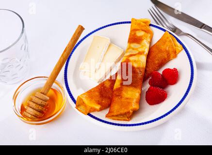 Crêpes au miel, framboises et tranches de fromage, servies sur assiette. Sur fond blanc. Banque D'Images