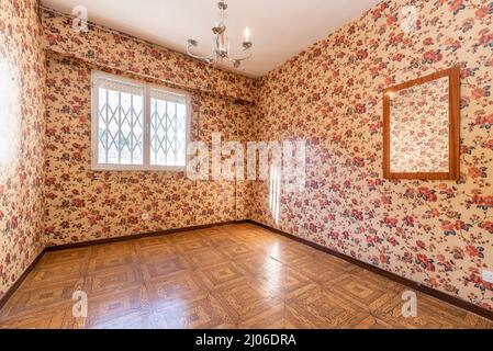 Cette chambre est dotée de murs tapissés de papier peint, de fleurs kitsch vintage et de sols en sintasol semblables à du parquet et de fenêtres avec des bars et un miroir au mur Banque D'Images