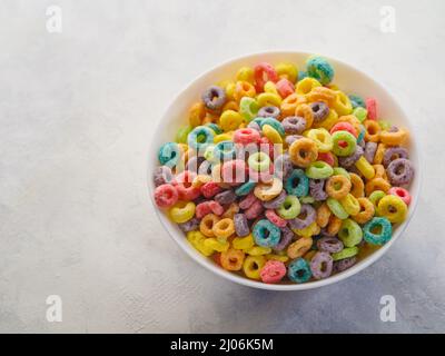 Des anneaux de maïs multicolores croustillants dans un bol sur fond blanc. Gros plan. Petit déjeuner rapide céréales, vitamines, nourriture saine, nourriture pour bébé. Banque D'Images