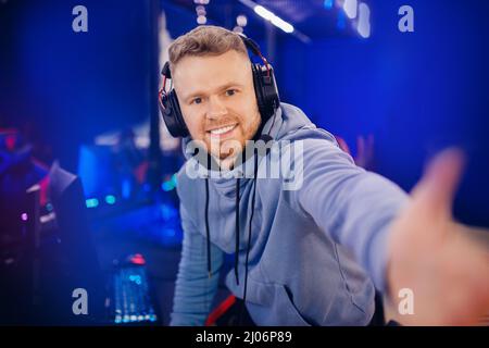 Streamer jeune homme joueur professionnel jouant en ligne jeux ordinateur avec casque faire selfie photo, couleur néon. Banque D'Images