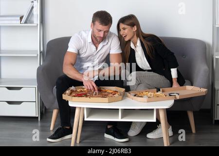 Une femme riant à une blague drôle, mangeant de la pizza avec des collègues de divers hommes au bureau, des employés heureux s'amusant ensemble pendant le déjeuner, appréciant le bien Banque D'Images