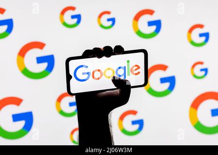 Smartphone avec le logo de la société de technologie Google sur l'écran dans une main trempée sur l'arrière-plan des logos Google Banque D'Images
