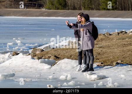 MINSK, BÉLARUS - 16 MARS 2022 : les filles prennent des selfies sur la rive du réservoir où la dérive de glace a commencé. Banque D'Images