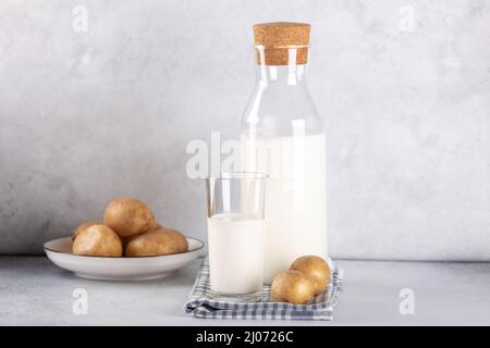 Boisson de pomme de terre sans lait en verre et en bouteille.Lait de pomme de terre de remplacement et tubercules de pomme de terre sur table grise.Copier l'espace Banque D'Images