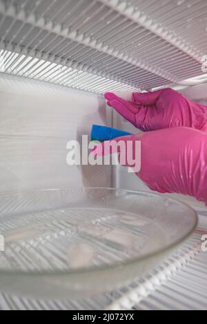 Dégivrage et nettoyage du congélateur. Une femme en gants de latex essuie l'eau de fonte avec une éponge. Faible profondeur de champ. Banque D'Images