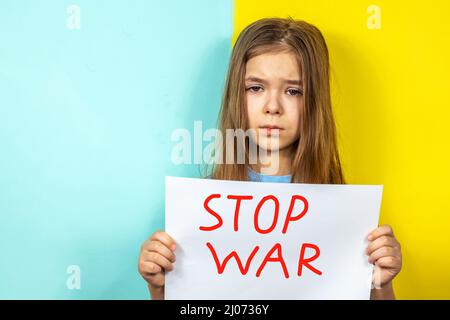 Une fille pleure, tenant une affiche D'ARRÊT DE GUERRE dans ses mains contre le fond du drapeau ukrainien. Arrêter la guerre en Ukraine. Le concept de paix Banque D'Images