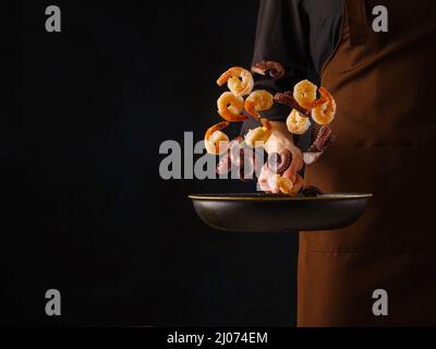 Le chef cuisine les crevettes et le poulpe avec vegetables.seun cocktail.rôtisserie de la poêle.congélation en mouvement.livre de cuisine et de recette.fond noir pour le texte Banque D'Images