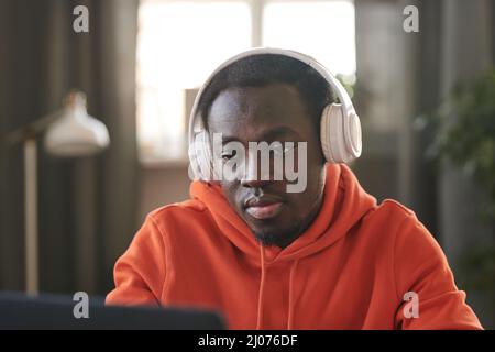 Portrait horizontal moyen en gros plan d'un beau jeune Africain américain portant un casque blanc surfant sur Internet sur un ordinateur portable Banque D'Images