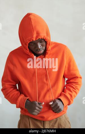 Portrait conceptuel de studio vertical moyen d'un jeune Africain américain portant un capuchon de serrage orange Banque D'Images