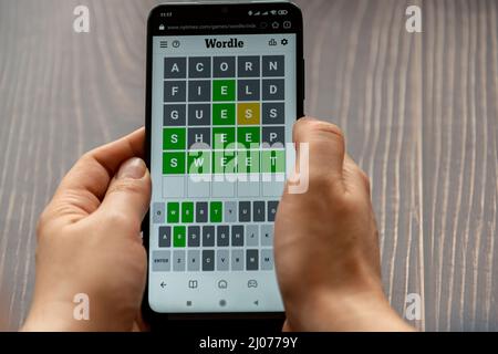 Mains de la personne tenant un téléphone jouant au jeu Wordle sur le site NYTimes.com Banque D'Images