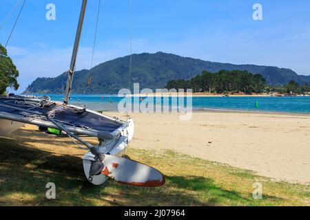 Catamaran sur la plage de Tairua, une ville balnéaire ensoleillée sur la péninsule de Coromandel, Nouvelle-Zélande. De l'autre côté du port se trouve la ville de Pauanui Banque D'Images