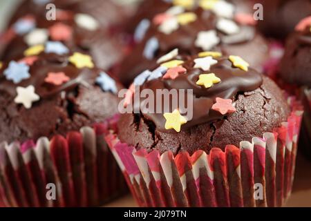 Gros plan de délicieux muffins au cacao faits maison (petits gâteaux) avec glaçage au chocolat noir et saupoudrés colorés en forme d'étoiles. Mise au point sélective Banque D'Images
