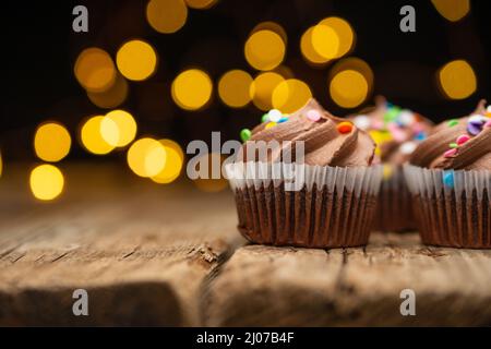 Cupcakes au chocolat avec arrosage sur fond de bois rustique avec des lumières jaunes. Dessert sucré. Concept de boulangerie. Cuisine élégante. Illustration du livre de recettes. Banque D'Images