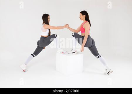 Deux jeunes femmes de fitness donnent poignée de main sur fond gris en studio Banque D'Images