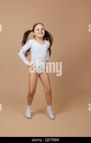 Portrait de jeune adorable heureuse fille souriante avec de longs cheveux foncés en blanc entraînement maillot de bain et chaussettes sautant sur fond marron, posant, ayant le plaisir Banque D'Images