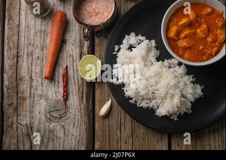 Vue rapprochée de l'assiette avec délicieux poulet tikka masala curry et riz sur une table rustique en bois avec fond d'épices. Plat indien traditionnel. Banque D'Images