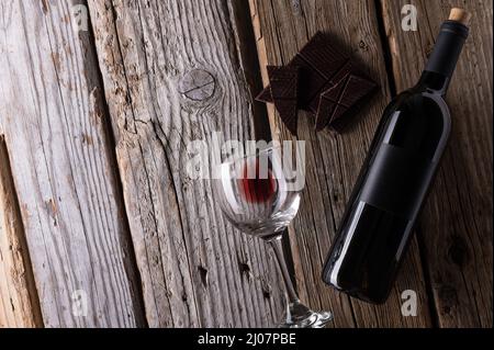 Composition fantastique avec chocolat noir, bouteille élégante et verre avec restes de vin rouge sur fond rustique en bois. Publicité et promotion co Banque D'Images