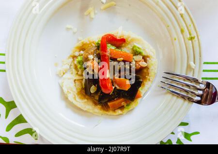 Arepa avec des légumes cuits sur une assiette en porcelaine avec une fourchette sur l'assiette et la table en arrière-plan, concept de cuisine, l'Amérique latine traditionnelle Banque D'Images