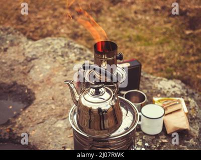 La théière se trouve sur le bord du samovar chromé de la pipe dont un feu brûle. Thé boire dans la nature le jour de l'automne Banque D'Images