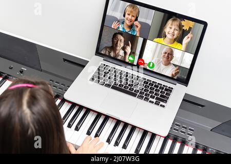 Une jeune fille apprend à chanter et à jouer du piano à partir d'une vidéo conférence à partir d'un ordinateur portable. Appels vidéo pour l'éducation, auto-éducation. Banque D'Images