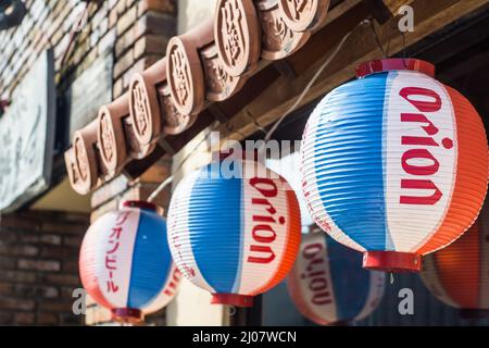 Gros plan de lanternes japonaises en papier à suspendre rouge, bleu et blanc faisant la promotion de la bière Orion devant un restaurant Okinawa à Nara, au Japon Banque D'Images