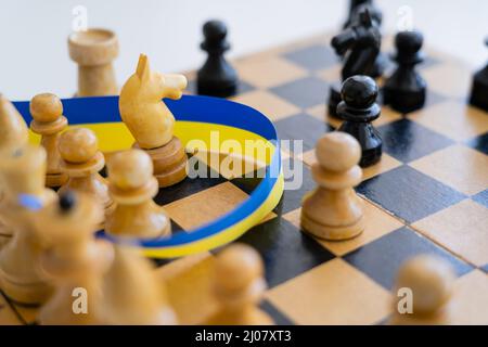 Vue rapprochée du ruban bleu et jaune près des figures d'échecs à bord isolées sur blanc Banque D'Images