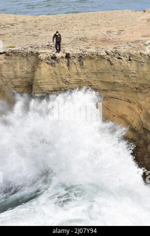 Grande vague s'écrasant sur des rochers, homme pêchant sur la haute falaise, sud-ouest de l'Alentejo et parc naturel de la côte de Vicentine dans le sud-ouest du Portugal. Banque D'Images