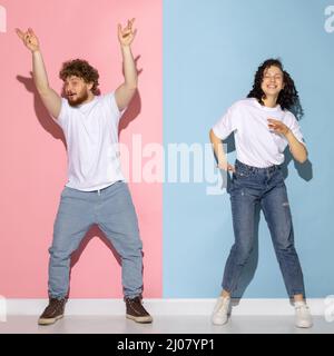 Couple émotionnel de jeunes drôle et heureux homme et fille dansant hip-hop en studio sur fond bleu et rose tendance couleur. Banque D'Images