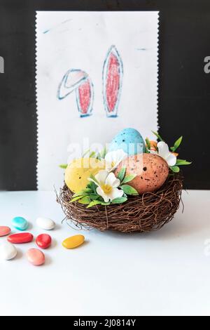 Œufs de Pâques dans un panier avec fleurs et chocolats sur fond blanc, gros plan Banque D'Images