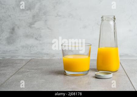 Bouteille et verre avec jus liquide jaune boisson halthy sur fond de béton gris. Orange frais Banque D'Images