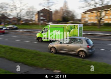 Asda en ligne à la maison de livraison de nourriture de livraison van conduite le long d'une route occupée en panoramique tourné avec l'espace de copie. Banque D'Images