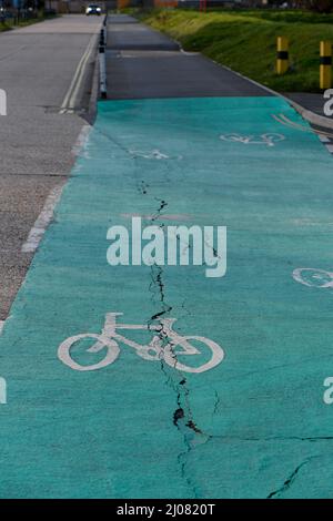 Colorer la trajectoire du cycle avec le logo de vélo avec des fissures et des dommages à la surface où la trajectoire traverse la jonction de la route. Banque D'Images