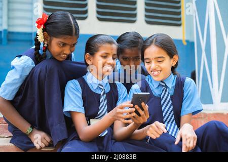 groupe de jeunes filles souriantes occupés à utiliser le téléphone mobile dans le couloir de l'école pendant la pause - concpet de la dépendance de smartphone, en utilisant les médias sociaux et Banque D'Images