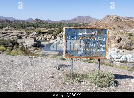 Vieux signe bleu rouillé avec un texte blanc d'avertissement en arabe en plein soleil à Wadi Al Hoqain, Oman Banque D'Images