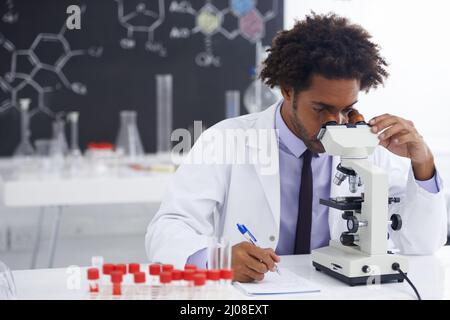 HMM, c'est un développement intéressant Cliché d'un biologiste mâle regardant une lame de verre à travers un microscope. Banque D'Images
