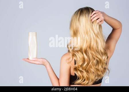 Femme cheveux longs. Une femme tient le shampooing et l'après-shampooing en bouteille. Femme tenant une bouteille de shampooing. Belle fille blonde avec une bouteille de shampoings dans les mains Banque D'Images