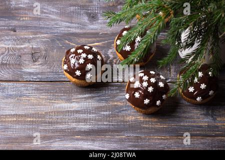 Muffins épicés à la citrouille aux noix, décorés de glaçage au chocolat et de flocons de neige sous l'arbre de Noël sur une table en bois, espace libre, sélectif Banque D'Images