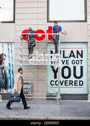 Milan, Italie. 03rd octobre 2019. Un homme d'affaires passe devant deux hommes travaillant sur un panneau d'affaires à Milan le 31 mars 2019. Corso Buenos Aires est l'une des plus longues rues commerçantes d'Europe et possède la plus grande concentration de magasins. (Photo par Alexander Pohl/Sipa USA) crédit: SIPA USA/Alay Live News Banque D'Images