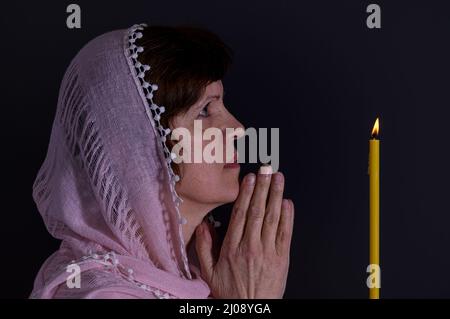 Portrait de la belle femme ukrainienne priant devant la bougie sur fond sombre. Banque D'Images