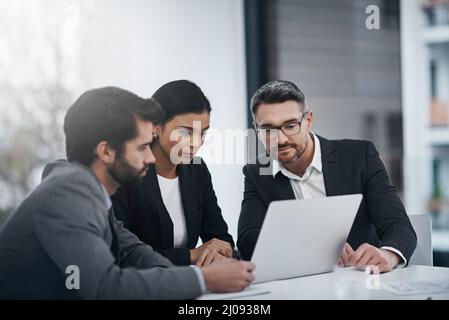 C'est une équipe qui fait les choses. Photo de trois hommes d'affaires réunis autour d'un ordinateur portable dans la salle de réunion. Banque D'Images