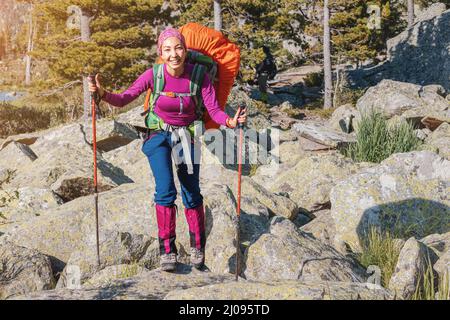 Une fille voyageur avec des bâtons de randonnée et un grand sac à dos marche le long d'un sentier parmi d'énormes pierres et des rochers dans un parc national Banque D'Images