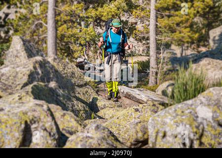 Le voyageur masculin avec des bâtons de randonnée et un grand sac à dos marche le long d'un sentier parmi d'énormes pierres et des rochers dans un parc national Banque D'Images