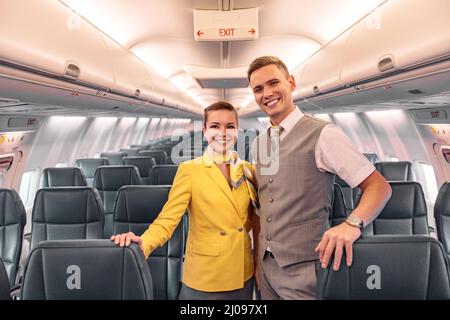 Les employés des compagnies aériennes qui se tiennent dans le salon de passagers de l'avion sont joyeux Banque D'Images