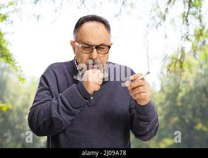 Homme mature fumant une cigarette et toussant dans un parc Banque D'Images