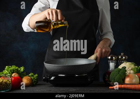 Un chef professionnel verse de l'huile d'olive dans une poêle pour cuire de la soupe sur fond bleu foncé. Coulisses de la préparation du repas. Plat sain. Concept alimentaire. F Banque D'Images