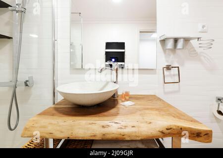 Image de face avec un lavabo blanc sur un comptoir en bois et une cabine de douche vitrée, un miroir carré blanc anti-buée Banque D'Images