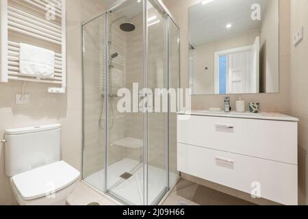 Salle de bains avec cabine de douche carrée avec cloison en verre, lavabo mural en porcelaine blanche, miroir rectangulaire et porte-serviette chauffant blanc Banque D'Images