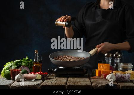 Vue macro d'un chef professionnel en uniforme noir verse les épices dans une poêle avec de la viande frite. Concept de tacos mexicains traditionnels Banque D'Images