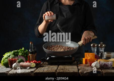 Vue macro d'un chef professionnel en sels noirs uniformes friture de viande dans la poêle. Arrière-plan de la cuisine traditionnelle mexicaine tacos. Concept de la cuisine Banque D'Images
